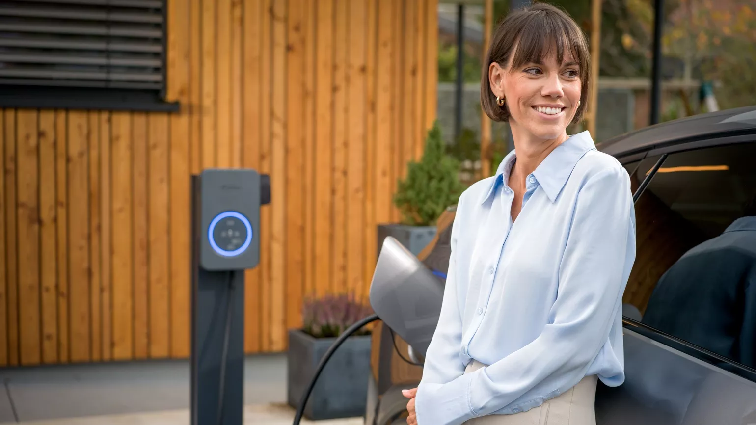 Woman leaning at her car while it is charging with Fronius Wattpilot Flex